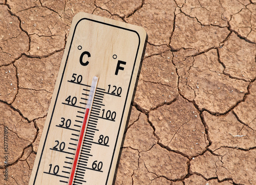 wooden thermometer shows hot temperature on dried cracked brown earth texture, concept of the consequences of climate change and the associated global warming