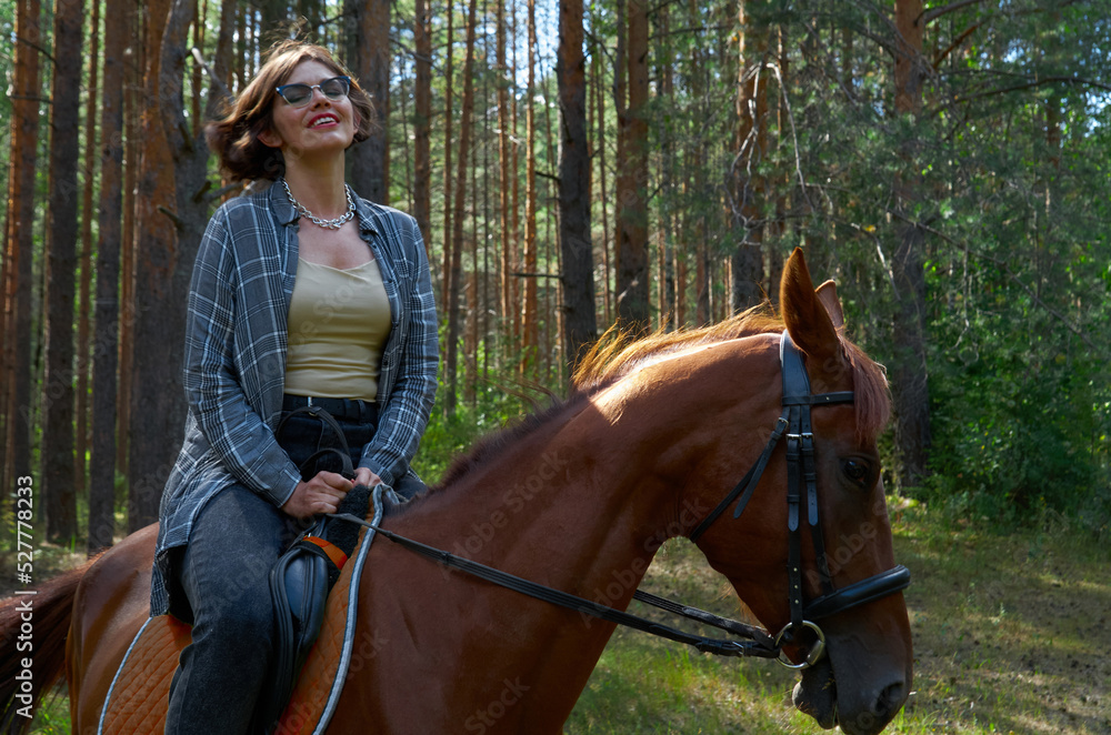 Obraz premium Woman in casual clothes rides a horse in hot summer day