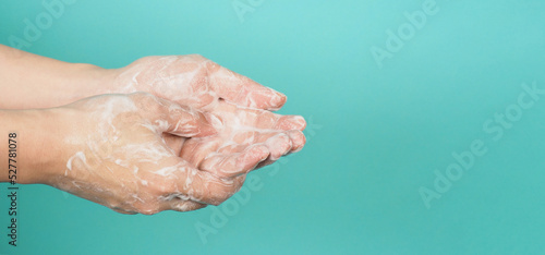 Hands washing gesture with foaming hand soap on mint green and Tiffany Blue background.