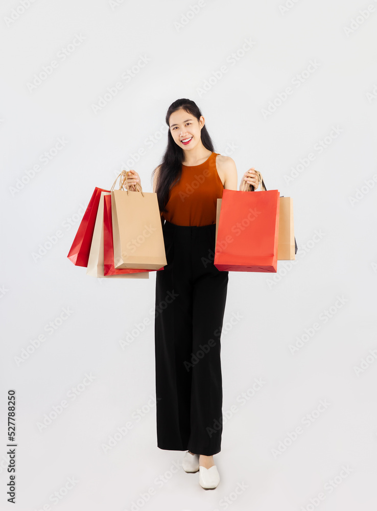 Pretty asian woman long hair carrying and holding red and brown paper shopping bags posing full body on white background.