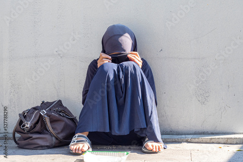 Muslim girl, woman sitting in a street of the city. Muslim woman with closed face begging for alms photo