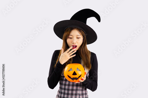 Young asian pretty woman in black halloween costume wearing witch hat and holding pumpkin lantern posing surprised and excited on white background.