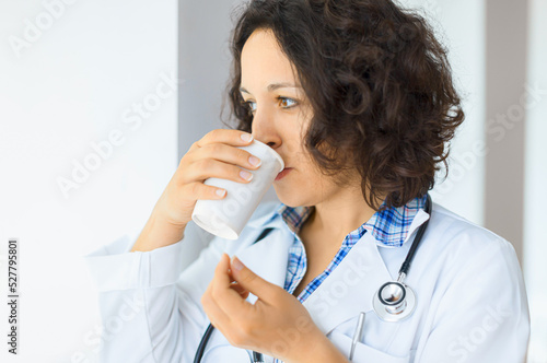 Doctor with stethoscope looking serious while drinking coffee