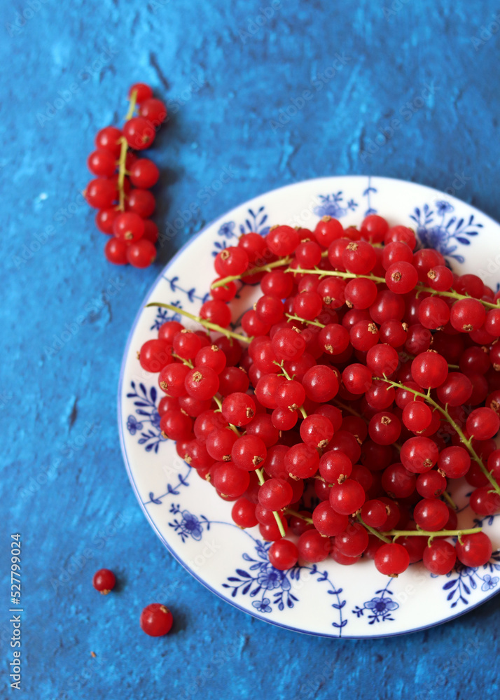 Red currant on blue ceramic plate. Blue texture background with copy space. Healthy eating concept. 