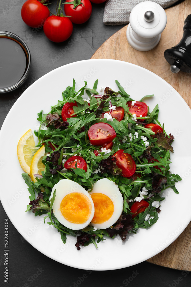Delicious salad with boiled egg, arugula and tomatoes served on black table, flat lay