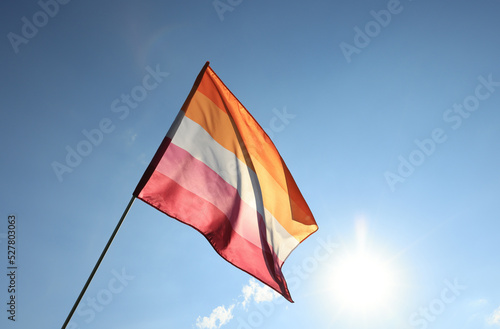 Woman holding bright lesbian flag against blue sky, space for text