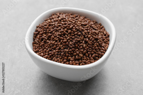 Buckwheat tea granules in bowl on light grey table, closeup
