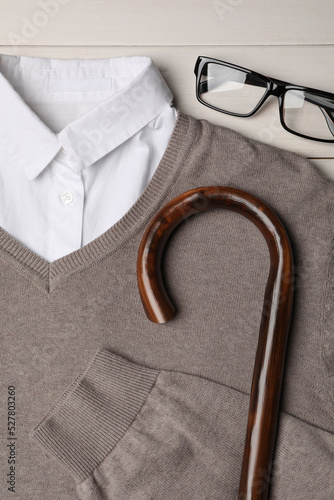 Elegant walking cane, sweater and glasses on white wooden table, flat lay
