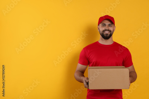 Courier holding cardboard box on yellow background, space for text photo