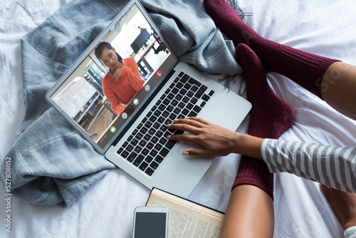Biracial young woman video conferencing with businesswoman while working from home on bed