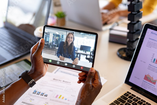 Cropped hands of african american man holding digital tablet while video calling female colleague
