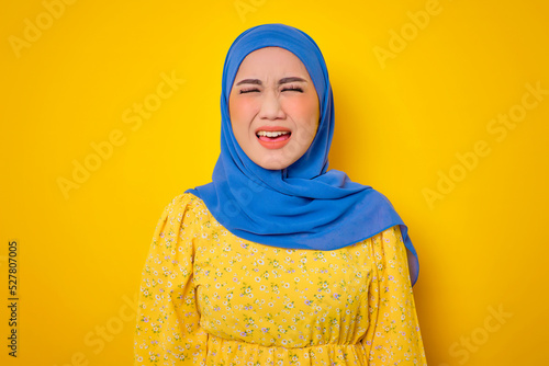 Angry young Asian woman in casual dress screaming with rage isolated on yellow background