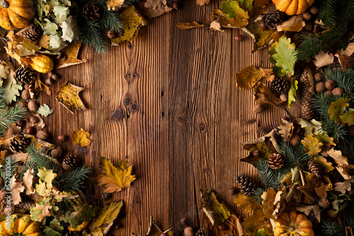Autumn composition on a rustic wooden background. Decorative pumpkins, various leaves, pine cones, nuts. Orange, yellow, red and brown aesthetics. 