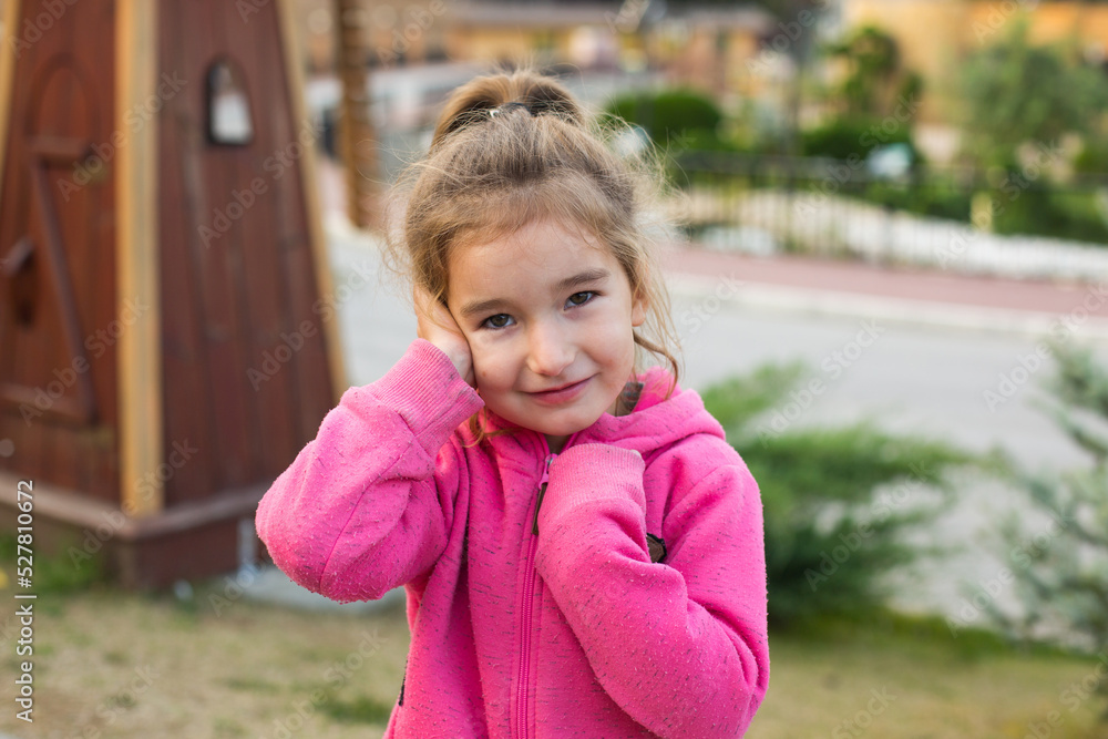 Poster Print A little girl in a pink hoodie with a sad and tearful face is holding her ear 40x26.7 cm