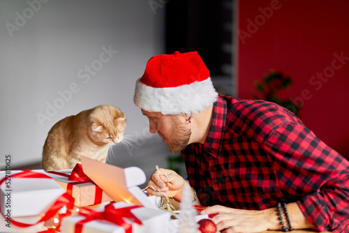 Vet Man in Santa hat and cat in hand making greeting card for New Year and Christmas