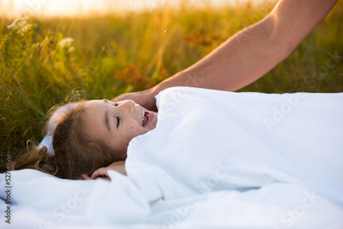 Girl sleeps on white bed in the grass, fresh air. Dad's hand gently pats his head. Care, protection, International Children's Day, mosquito bites