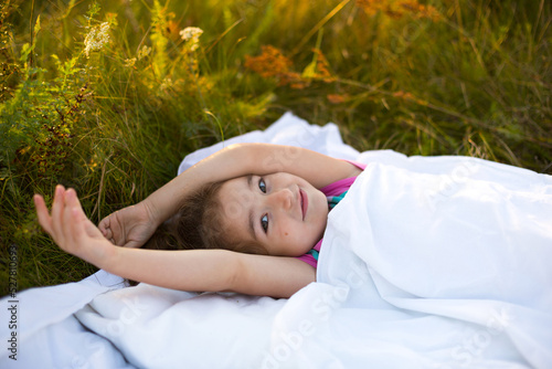 Girl sleeps on bed in grass, Sweet stretches and yawns sleepily, good morning in fresh air. Eco-friendly, healthy sleep, Protection from mosquitoes, clean nature, ecology, children's health