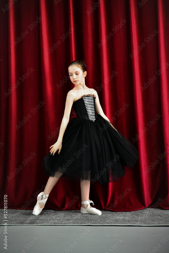 A cute ballerina girl in a black dress on a red background. Art. Dance. Beauty.