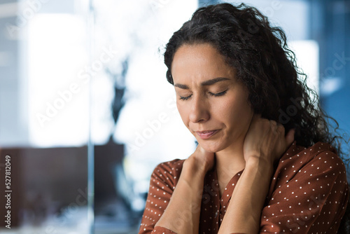 Fotografía Hispanic woman overtired working in modern office businesswoman has severe neck pain, massages neck muscles, business woman in casual clothes and curly hair