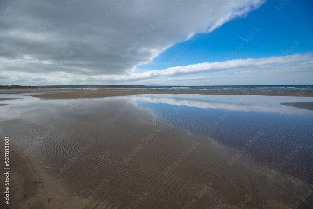 belle vue sur une plage avec les nuages et le ciel bleu qui se reflètent sur le sable mouillé