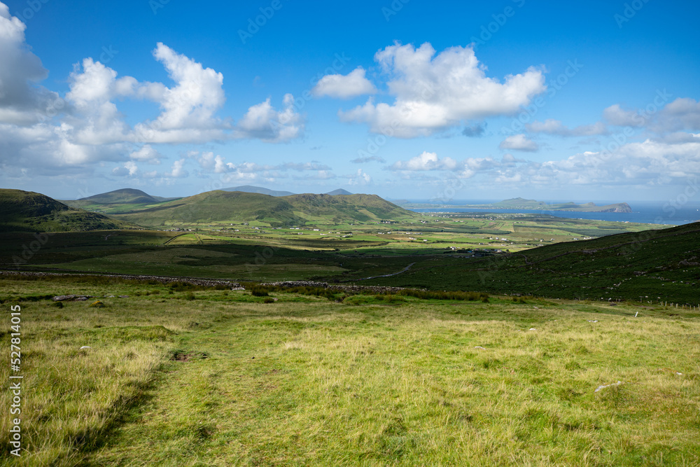 Vue spectaculaire montrant un paysage d'Irlande avec des collines, des prairies vertes et la mer, un ciel ensoleillé et nuageux