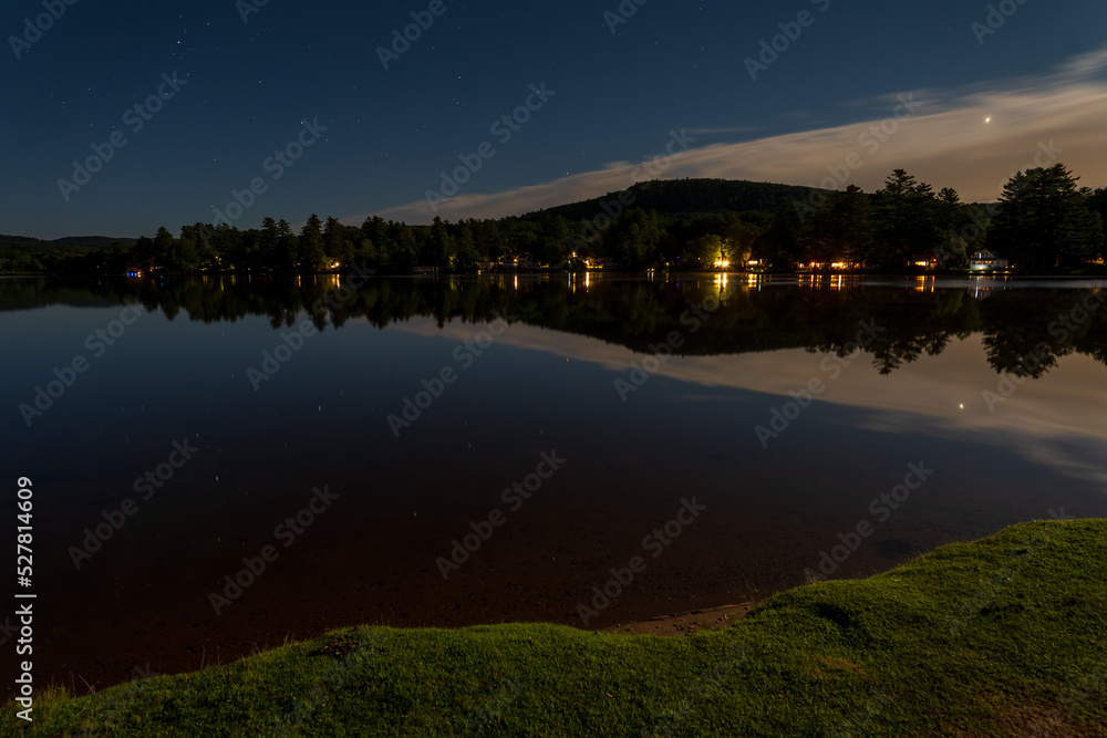 Nightscape image of a lake in New England. High quality photo was taken at night with a full moon with stars reflecting on a perfectly calm pond in New England. 