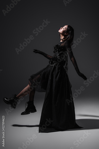 side view of asian young woman in black gothic dress and boots levitating on dark grey.