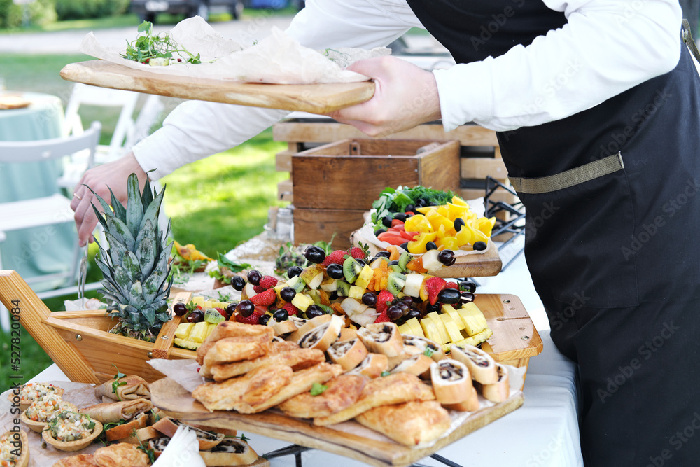 Waiter places food from one plate to another. Catering service. Wedding welcome food. Fruits on skewers and canapes.