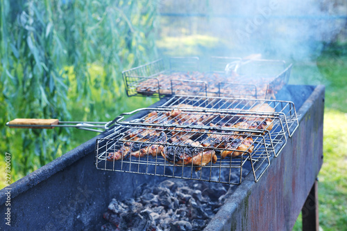 bbq chicken wings and chicken breast in a grill basket grid roasting and cooking on fire and smoke in a barbecue brazier