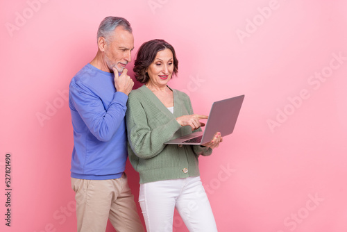 Photo of two positive aged persons hold use wireless netbook isolated on pink color background