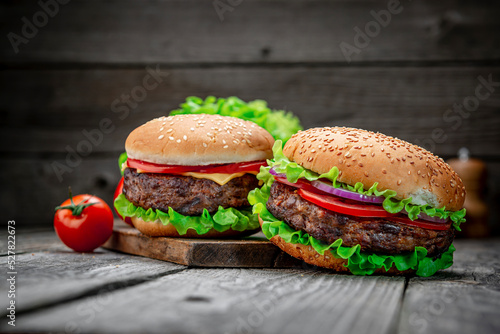 Two delicious homemade burgers of beef on an old wooden table. Fat unhealthy food close-up.