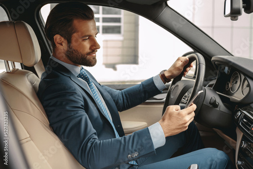 Happy Caucasian male in formal wear driving an automobile and holding smartphone in hand © Friends Stock