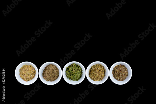 dried herbs for Mediterranean cooking in white bowls on a black background