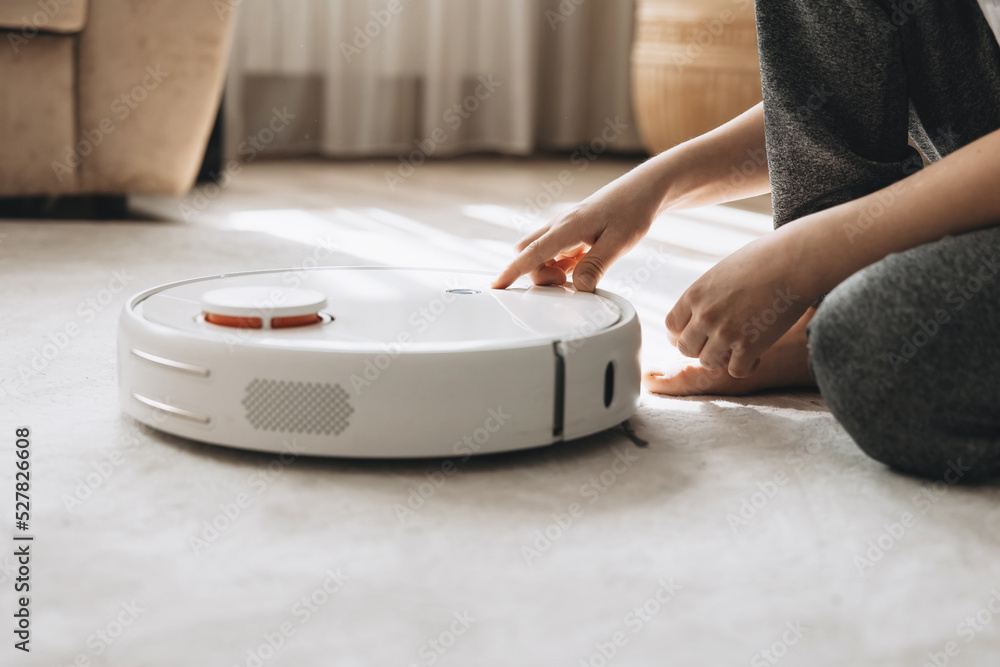 Fototapeta premium Child hand turn on smart robot vacuum cleaner. Modern smart device cleaning floor and carpet. Kid using wireless technology.