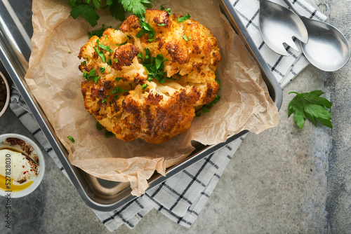 Baked cauliflower. Oven or whole baked cauliflower spices and herbs server on wooden rustic board on old grey background table. Delicious cauliflower. Eyal Shani dish. Perfect tasty snack. photo