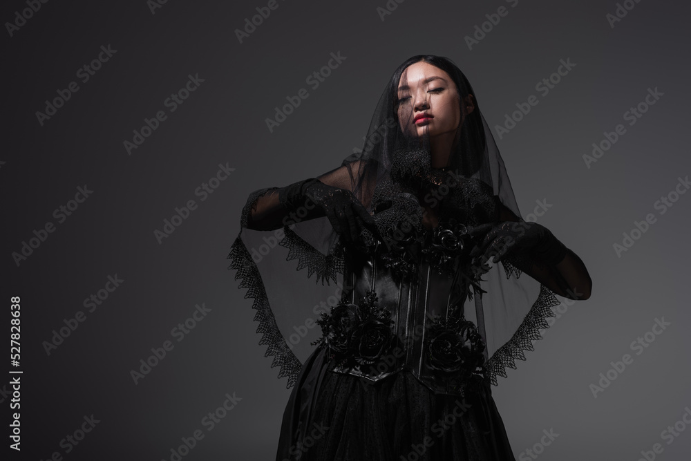 young asian woman in gothic outfit with black veil posing isolated on grey.