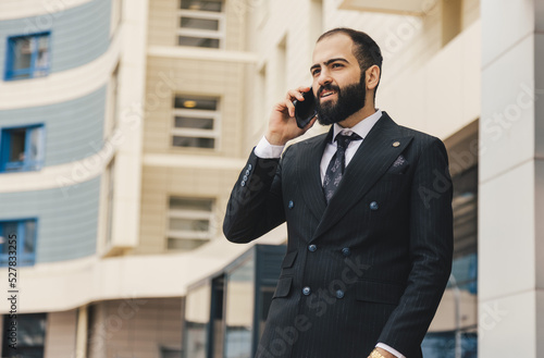 Portrait of a business man outdoors using the phone against the backdrop of a glass building downtown.