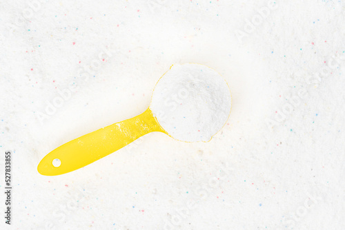 Laundry detergent for washing machines and a plastic scoop for dosing. Washing powder with measuring spoon. White wash powder with with colored granules