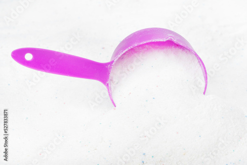 Laundry detergent for washing machines and a plastic scoop for dosing. Washing powder with measuring spoon. White wash powder with with colored granules