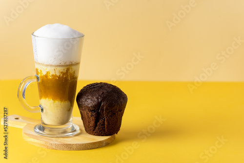 Pumpkin Spice Latte in a Glass Mug with Cinnamon on Wooden Cutting Board Chocolate Muffin Tasty Autumn Drink Yellow Background
