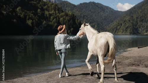 Back view young woman met a wild stallion on vacation in the mountains on a lake Amazing view turquoise water high mountain lake Braies mountains. Casual boho style clothing back view