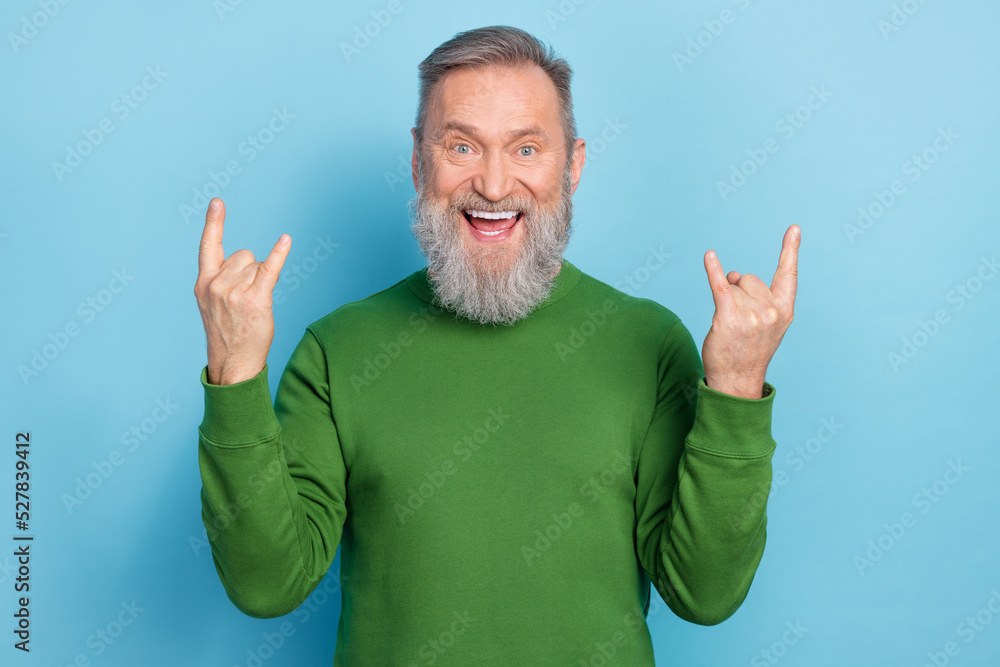 Photo of excited middle aged man making rock symbol punk performance visit isolated on blue color background Photo of excited middle aged man making rock symbol punk performance visit isolated on blue color background