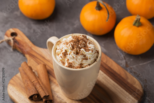 Autumn pumpkin spice latte with cream in mug on dark table. Traditional Coffee Drink for Autumn Holidays. A table decorated with pumpkins. Thanksgiving day or Halloween holiday. Fall time.