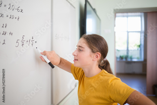 teenager child student thinks over solves example problem with fractions on blackboard in school classroom in math algebra lesson.