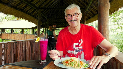 aktiver Senior genießt fröhlich sein Essen in einem Restaurant auf Stelzen über dem Dschungel von Bali photo