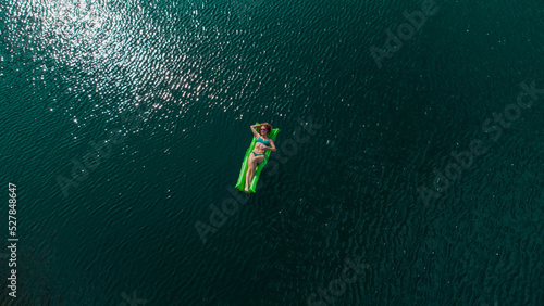 Happy girl swims in a green lake on a green mattress. curly beautiful girl swims. The girl is resting on the sea. Green mattress in the sea. The girl smiles and lies on the mattress. drone photo. Girl