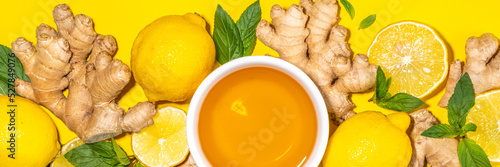 Healthy organic vegan immunity booster, herbal drink. Antioxidant anti-inflammatory ginger lemon tea with ingredient - fresh ginger, lemon, mint, bright yellow background flatlay top view copy space photo