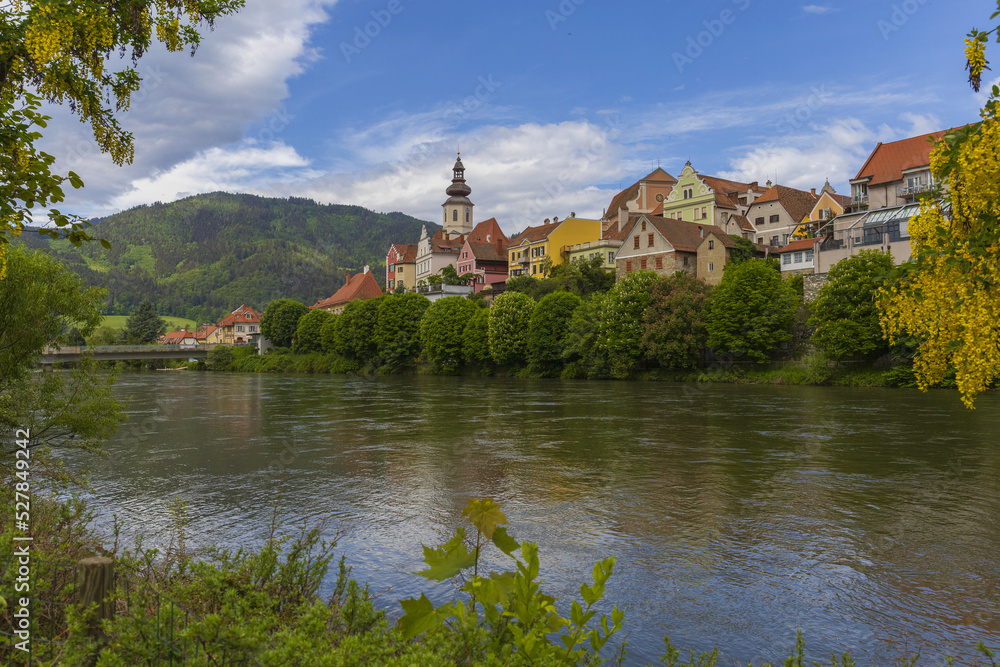 View to medieval Austrian village across a river on summer sunny day, pastoral Alpine panoramic landscape