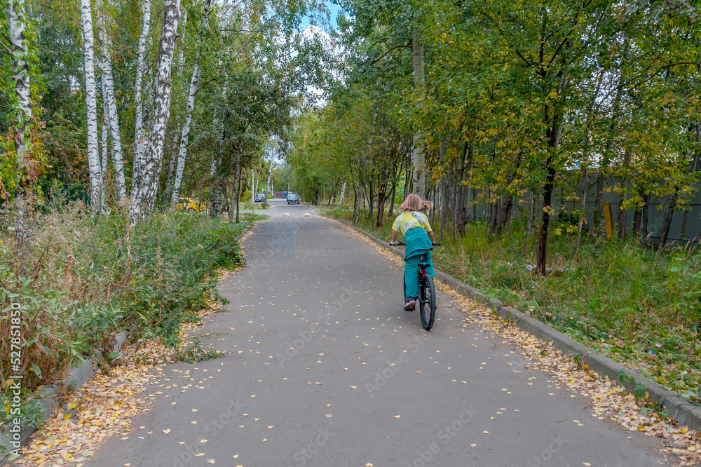 Alley with fallen leaves on which a girl rides a bicycle