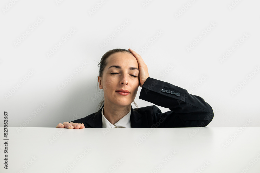 Young woman holding her head with closed eyes peeks out from behind a white cardboard on a white background Young woman holding her head with closed eyes peeks out from behind a white cardboard on a white background